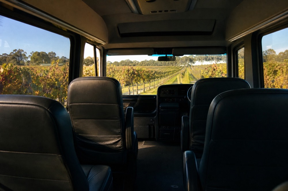 An air-conditioned tour vehicle interior with empty leather seats and a view of vineyard rows through the windscreen, soft daylight, no branding or people.